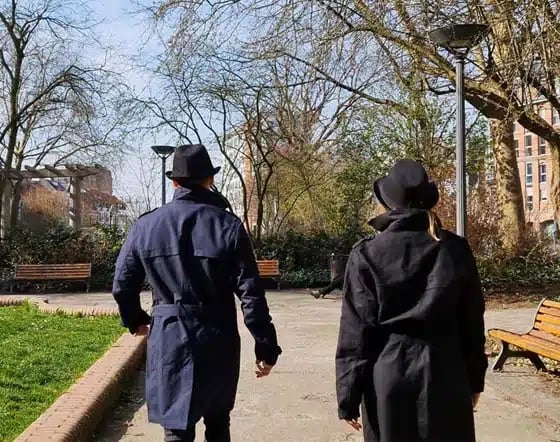 Deux joueurs en chapeau et trench-coat traversent un parc pendant une mission d'agents secrets de l'enseigne John Doe